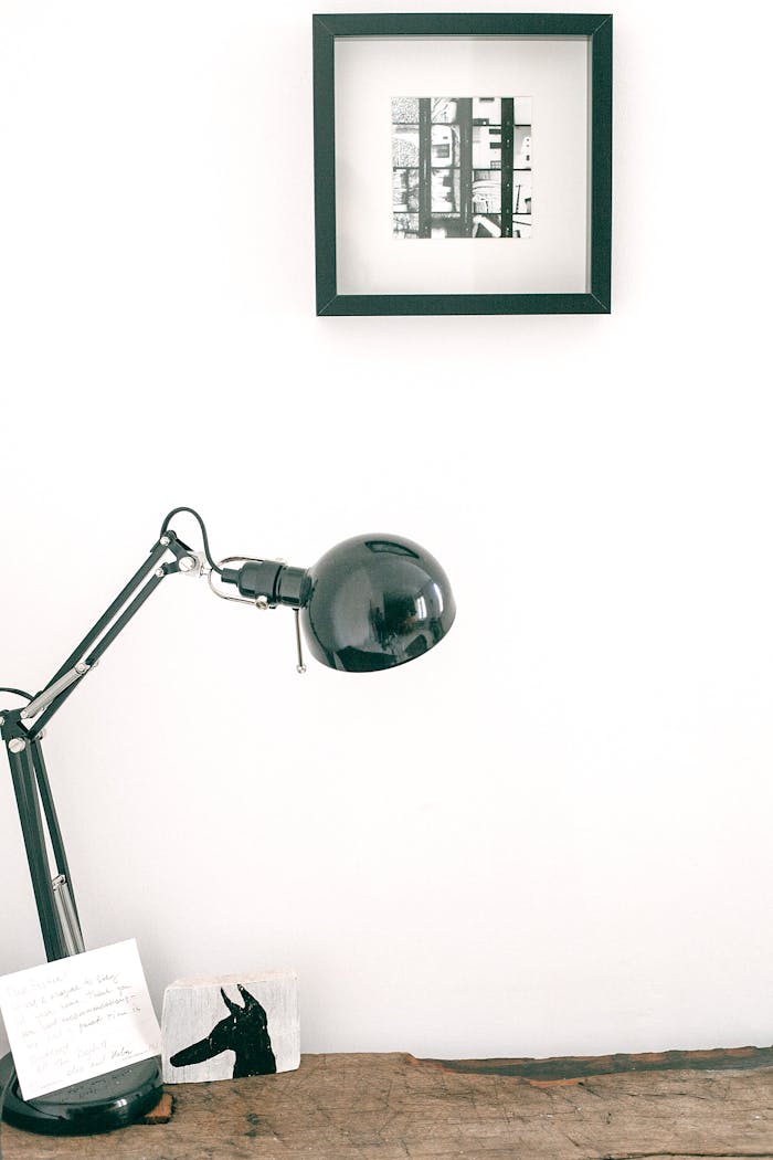 Modern black desk lamp with note placed on wooden table against white wall with picture in light room of cozy apartment