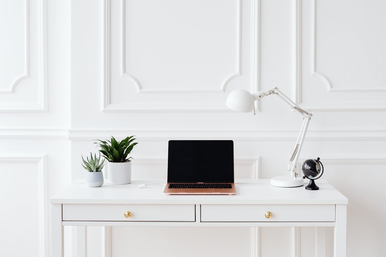 A minimalist home office setup featuring a laptop on a white desk with decor items.